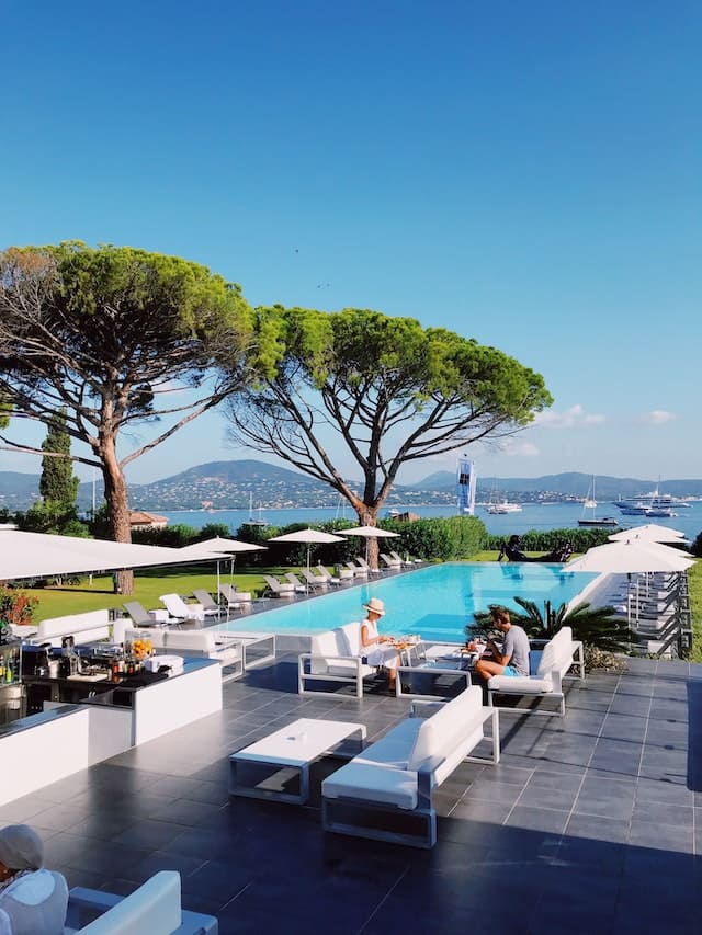 A pool with several sun loungers and two tress